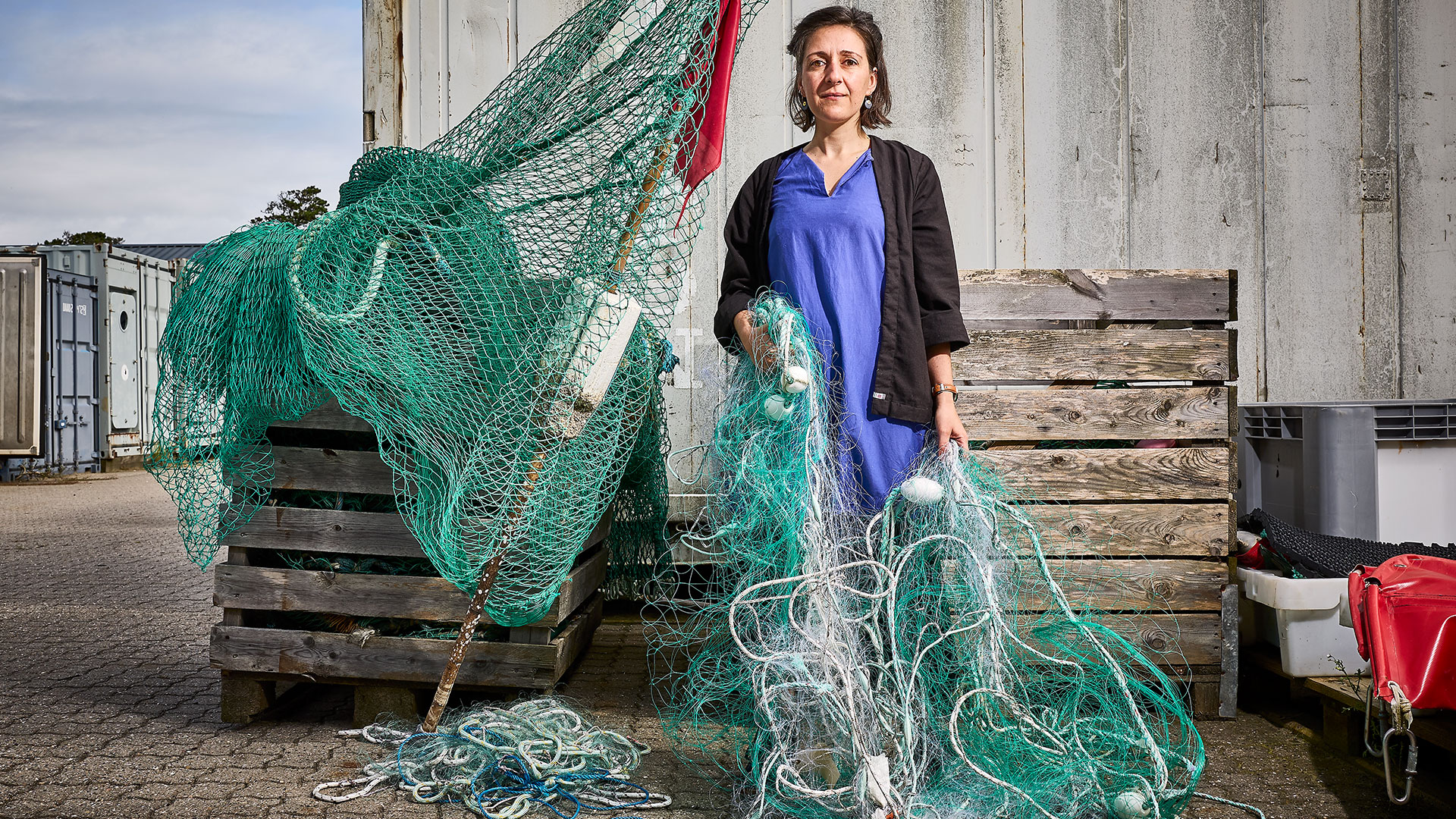 Kvinde står med fiskenet i hånden omgivet af fiskekasser. Foto: Claus Bjørn Larsen